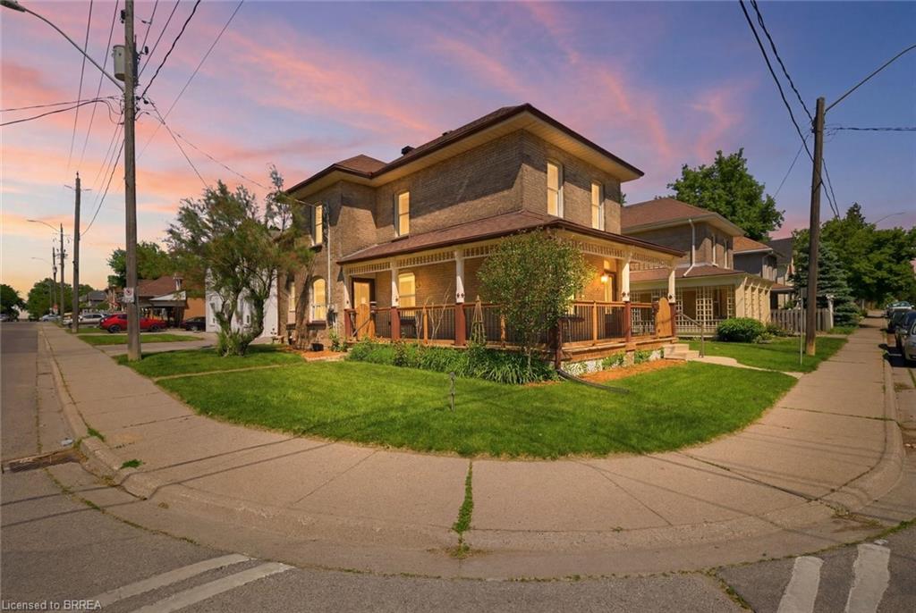 Twilight exterior of the brick Victorian home glowing under a pink sunset sky on its corner lot